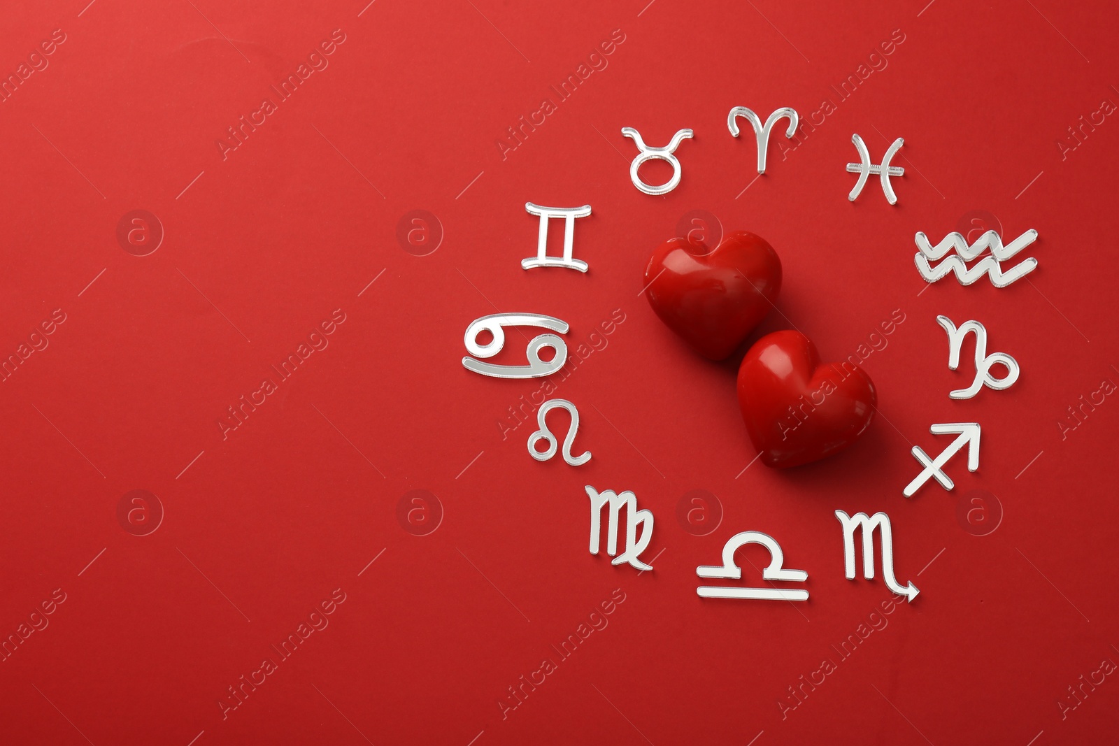 Photo of Zodiac signs and hearts on red background, flat lay. Space for text