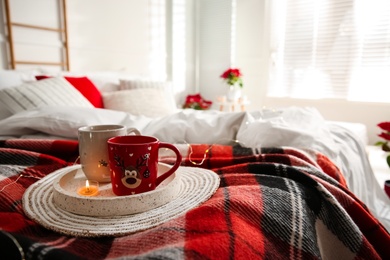 Photo of Christmas cups in tray on red woolen blanket. Bedroom interior