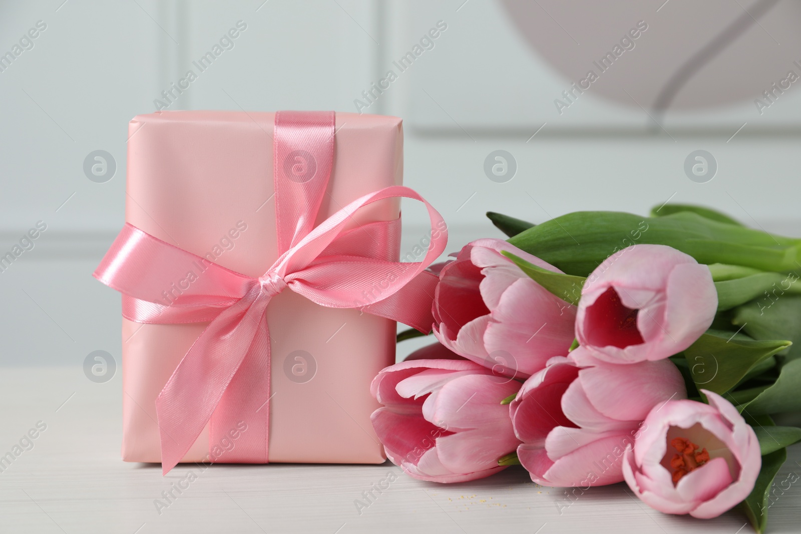 Photo of Beautiful gift box with bow and pink tulips on white table, closeup