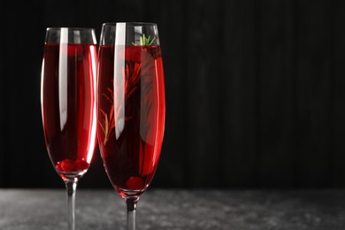 Photo of Tasty cranberry cocktail with rosemary in glasses against dark background, closeup. Space for text
