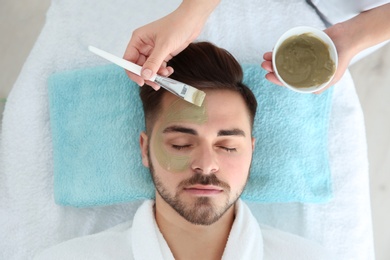 Cosmetologist applying mask on client's face in spa salon, above view