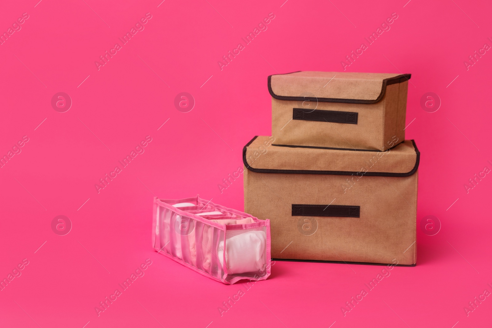 Photo of Textile storage cases and organizer with folded clothes on pink background. Space for text