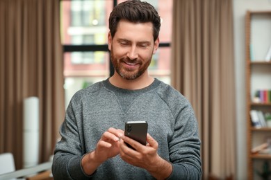 Photo of Handsome man sending message via smartphone indoors
