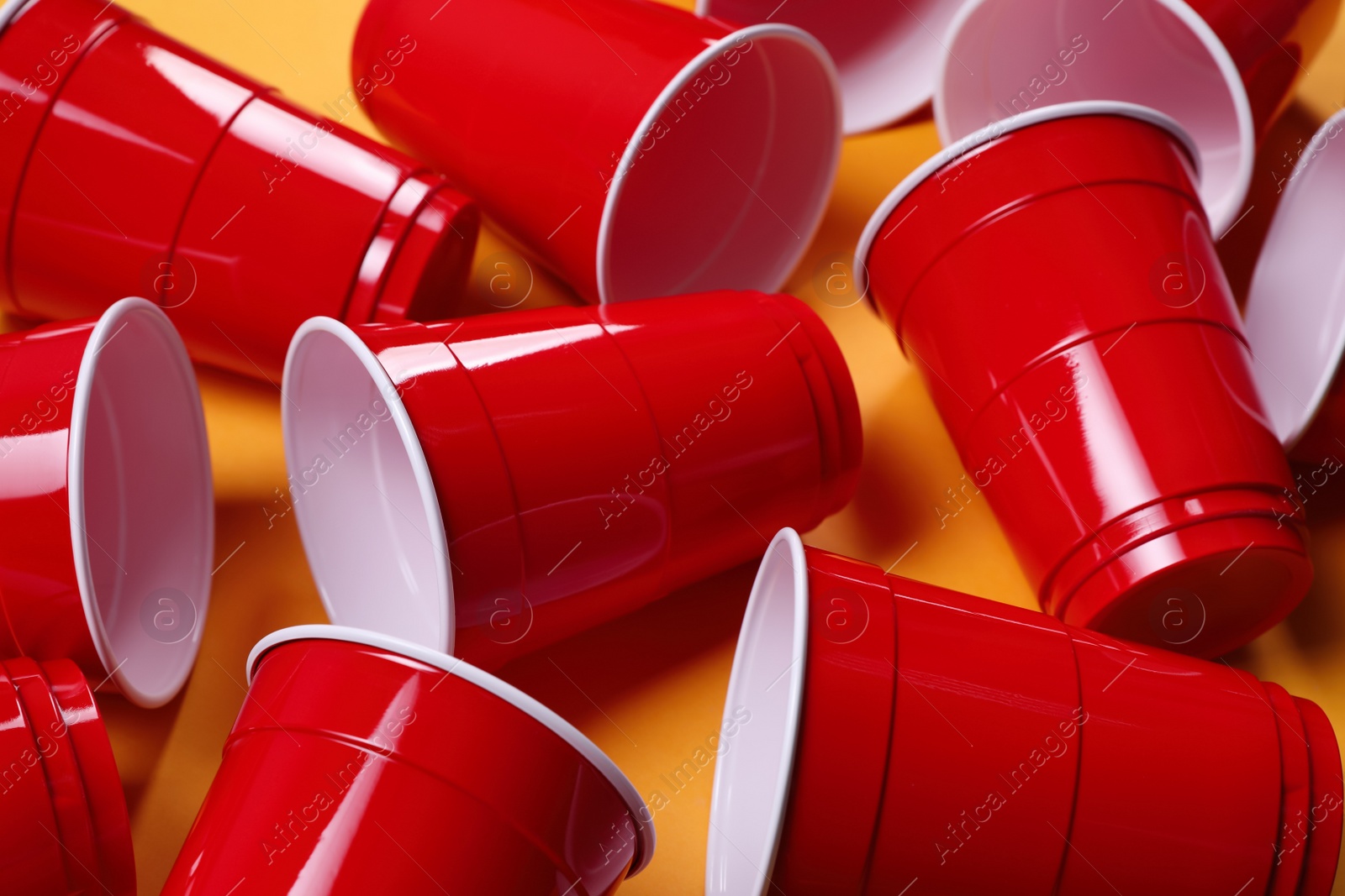Photo of Red plastic cups for beer pong game on orange background, closeup
