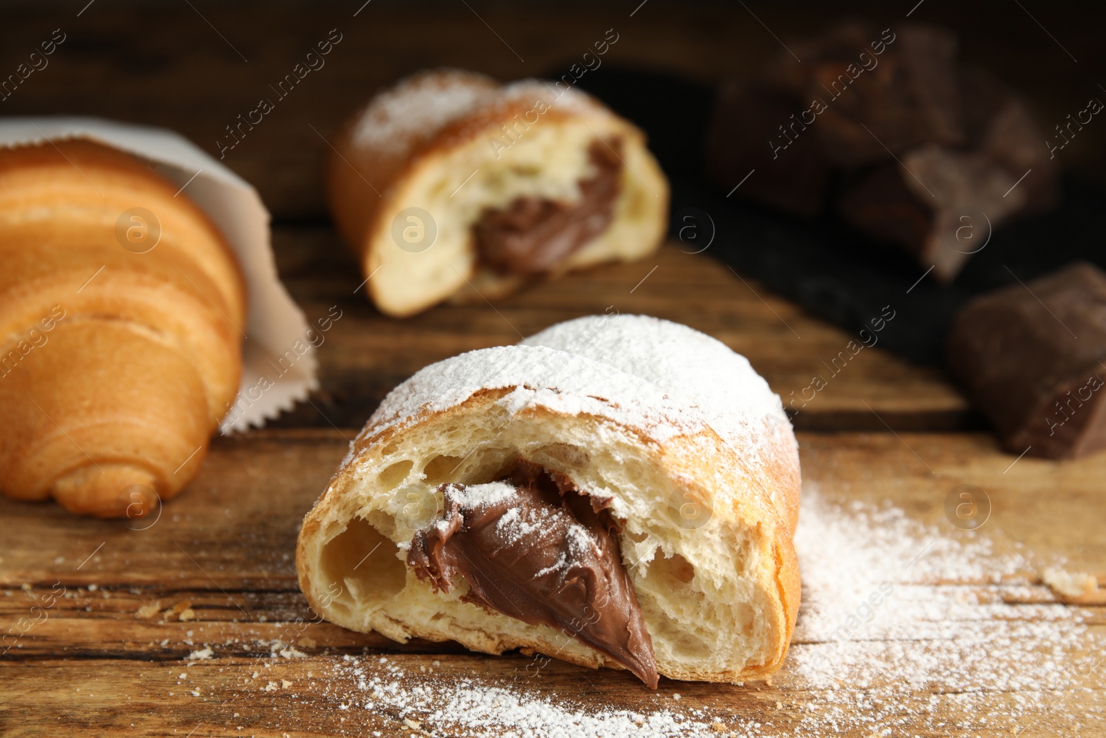 Photo of Tasty croissant with chocolate and sugar powder on wooden table. Space for text