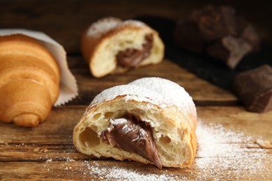 Photo of Tasty croissant with chocolate and sugar powder on wooden table. Space for text