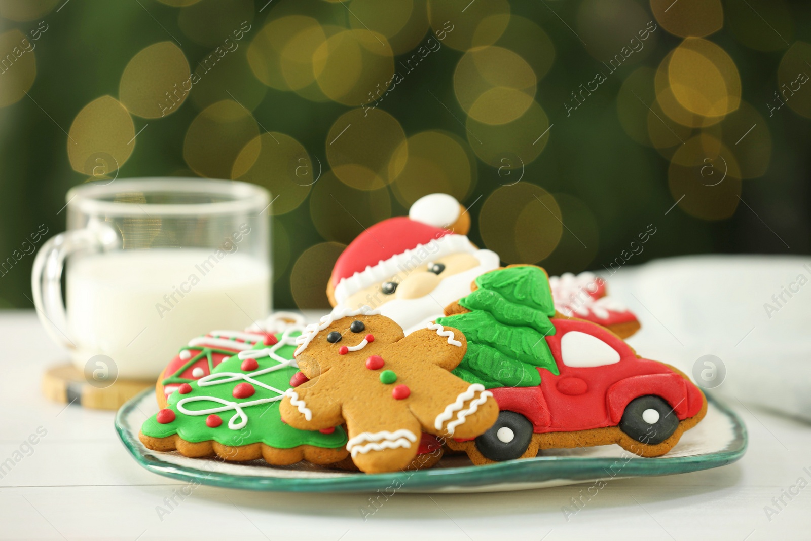 Photo of Decorated cookies and milk on white against blurred Christmas lights
