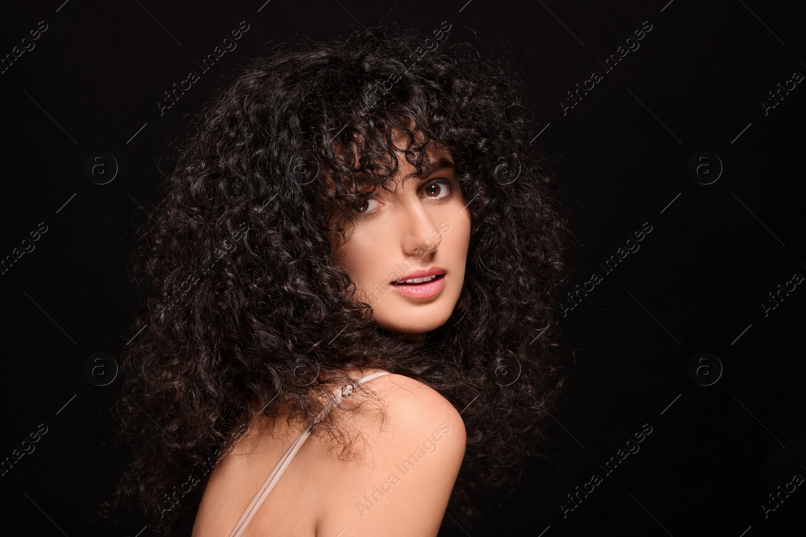 Photo of Beautiful young woman with long curly hair on black background. Space for text