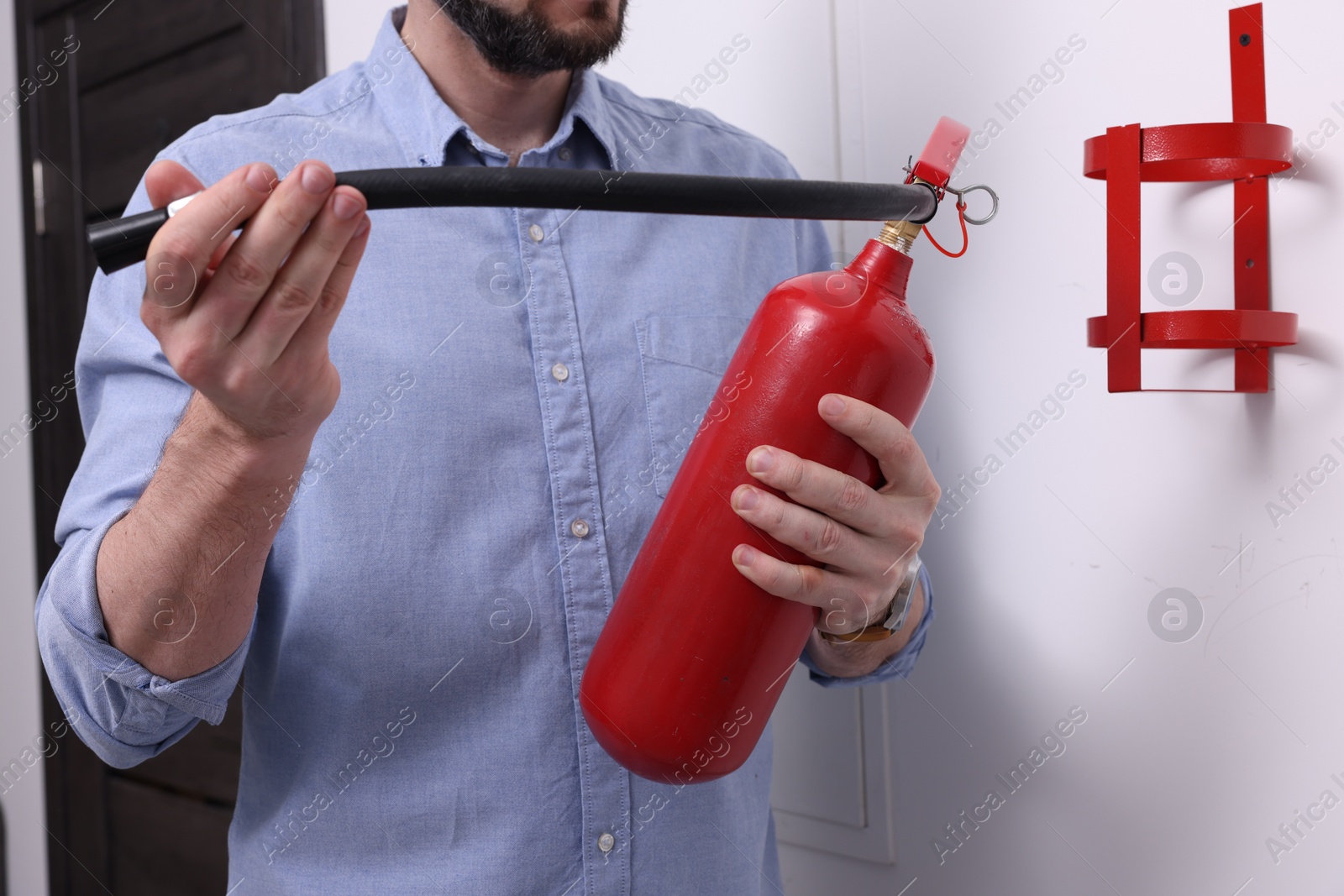 Photo of Man checking quality of fire extinguisher indoors, closeup