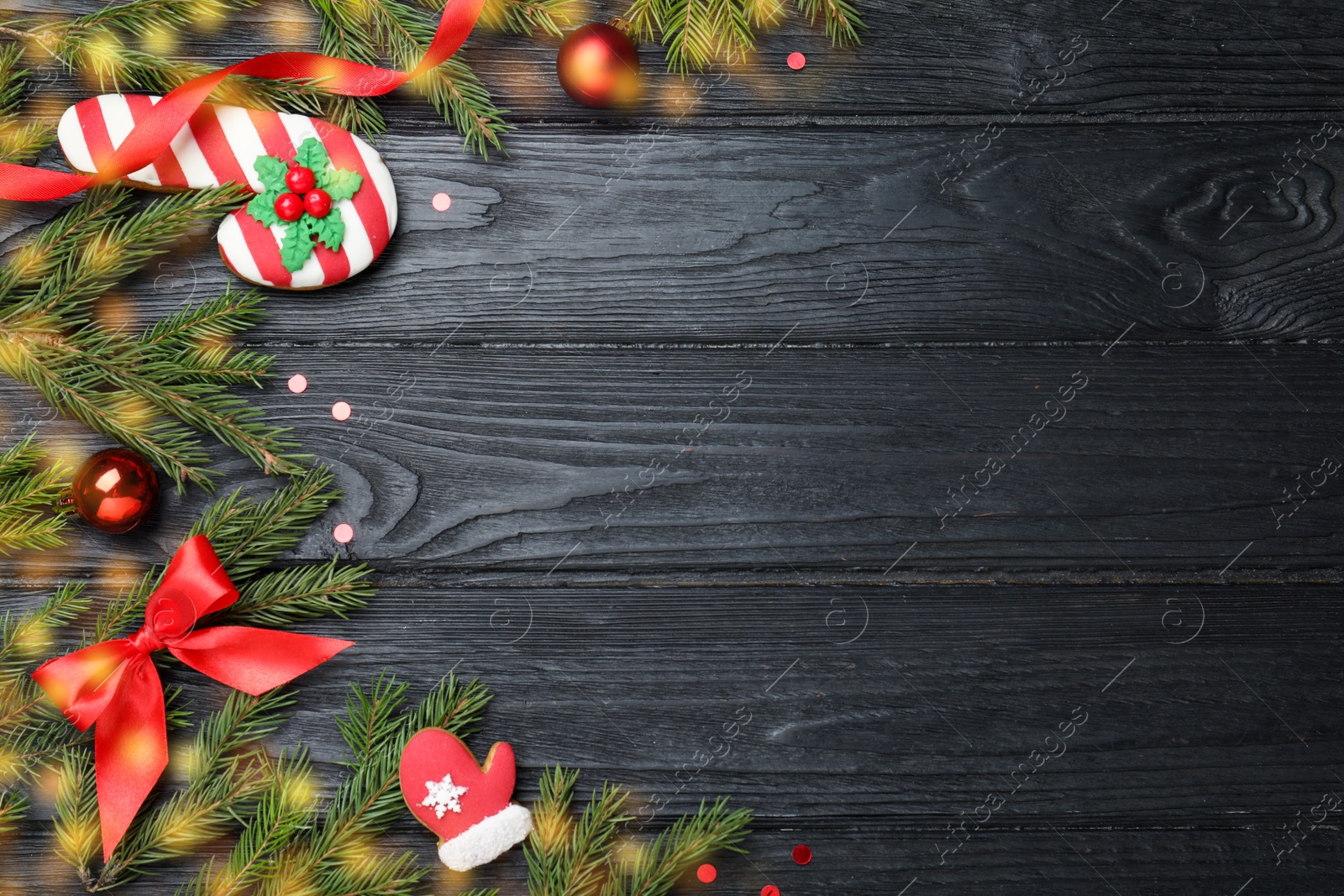 Photo of Christmas greeting card with space for text. Flat lay composition of fir tree branches and festive decor on black wooden background