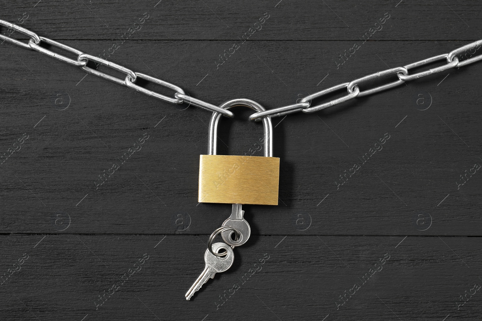 Photo of Steel padlock with keys and chain on black wooden table, top view