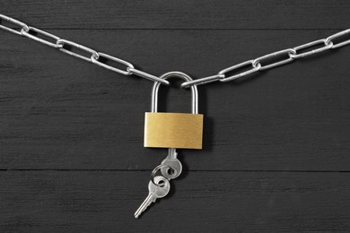 Steel padlock with keys and chain on black wooden table, top view