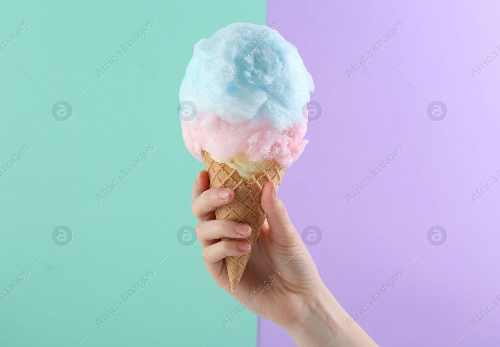 Photo of Woman holding waffle cone with cotton candy on color background, closeup