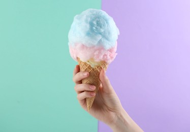 Photo of Woman holding waffle cone with cotton candy on color background, closeup