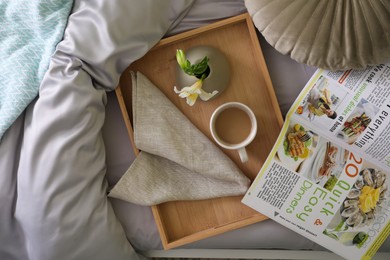 Photo of Tray with cup of coffee, flower and magazine on fresh bed linens, top view