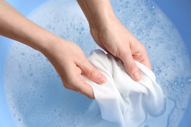 Photo of Top view of woman hand washing white clothing in suds, closeup