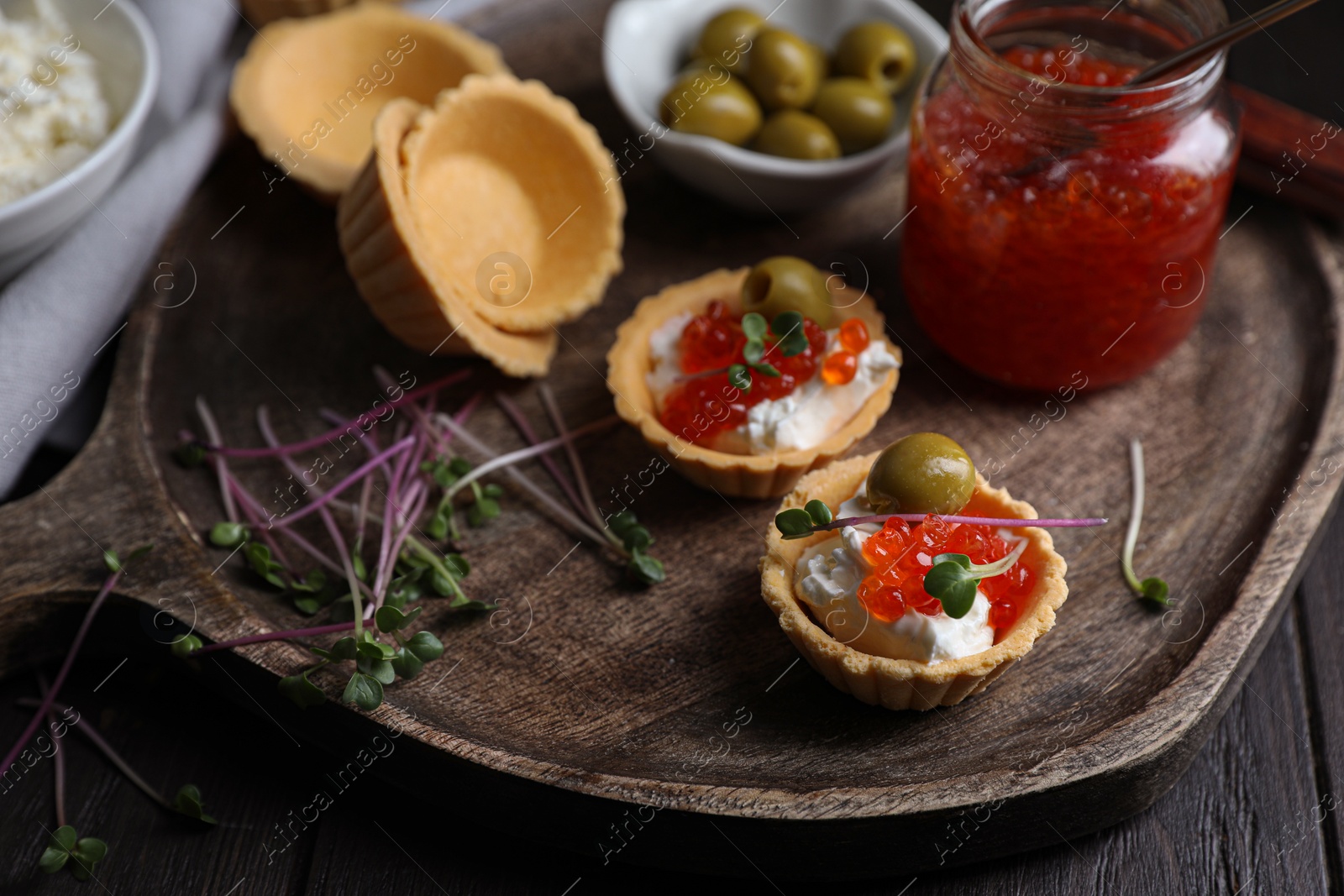 Photo of Delicious tartlets with red caviar and cream cheese served on wooden table, closeup