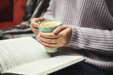 Photo of Woman with cup of coffee reading book at home, closeup