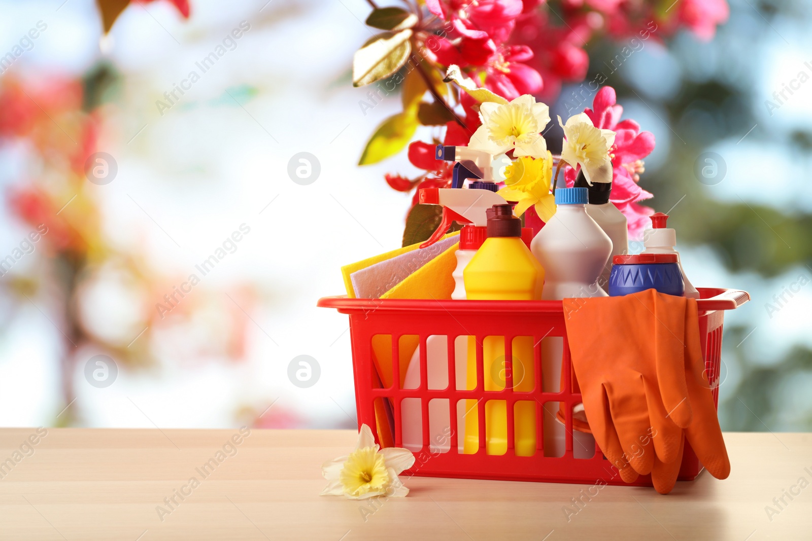 Image of Plastic basket with different detergents on wooden table, space for text. Spring cleaning concept 