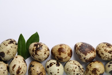 Photo of Speckled quail eggs and green leaves on white background, flat lay. Space for text