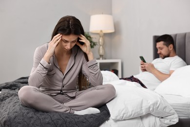 Stressed wife after quarrel with her husband sitting on bed, selective focus. Relationship problems