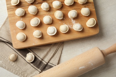 Photo of Board with raw dumplings and rolling pin on light background, flat lay. Process of cooking
