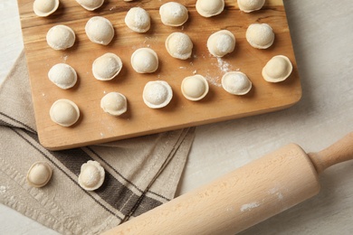 Board with raw dumplings and rolling pin on light background, flat lay. Process of cooking