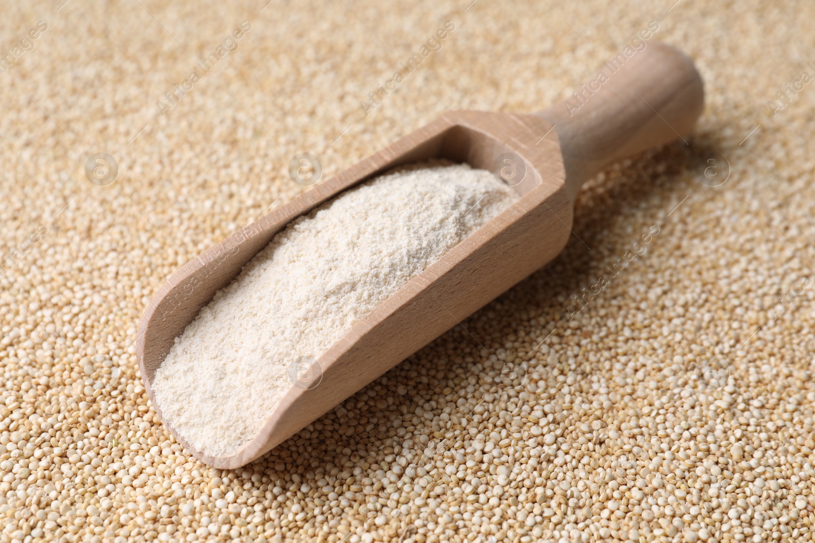 Photo of Wooden scoop with quinoa flour on seeds, closeup