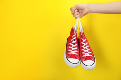Photo of Woman holding pair of sneakers on yellow background, closeup. Space for text