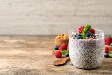 Photo of Delicious chia pudding with berries, granola and mint on wooden table, space for text