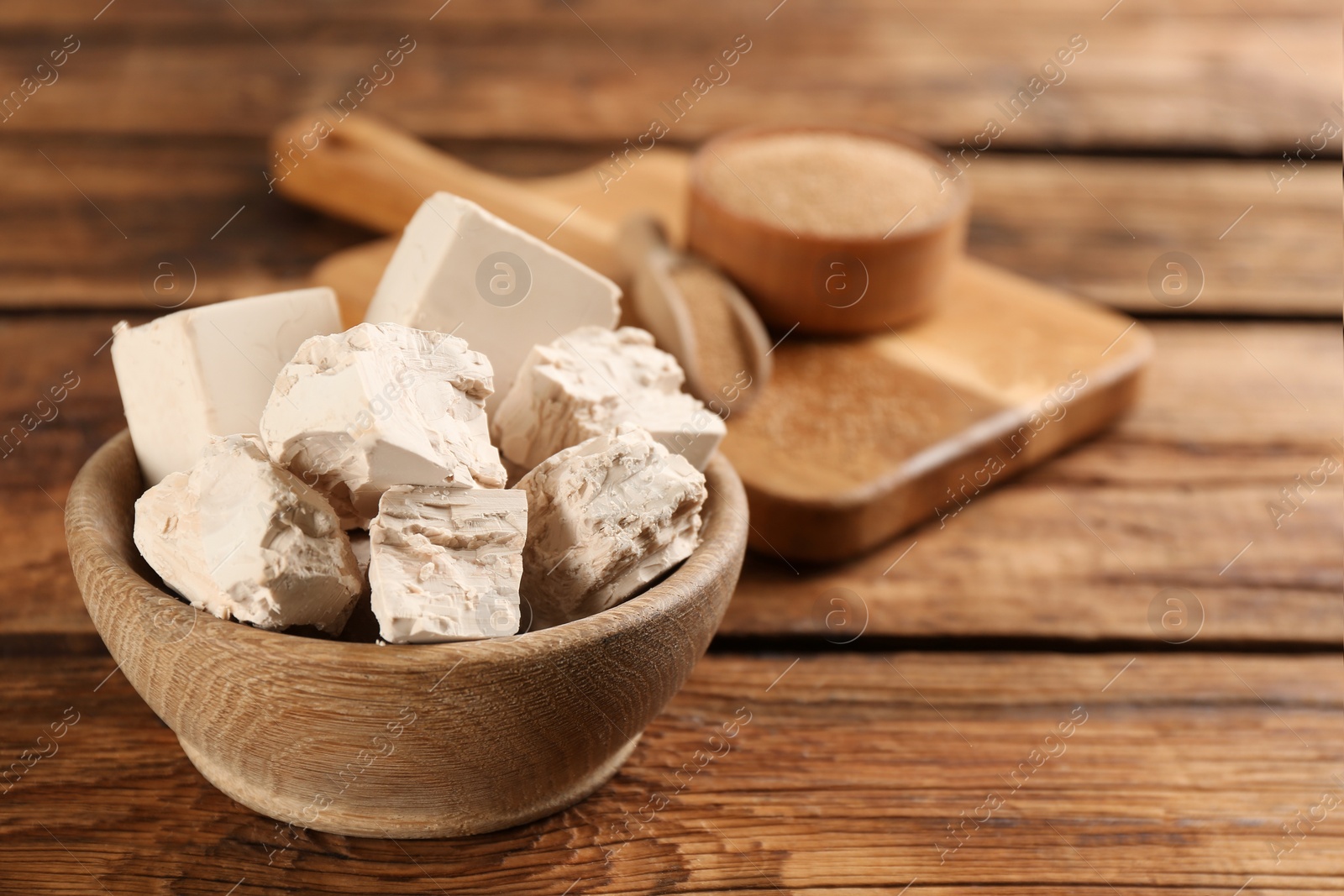 Photo of Bowl with pieces of compressed yeast on wooden table, closeup. Space for text