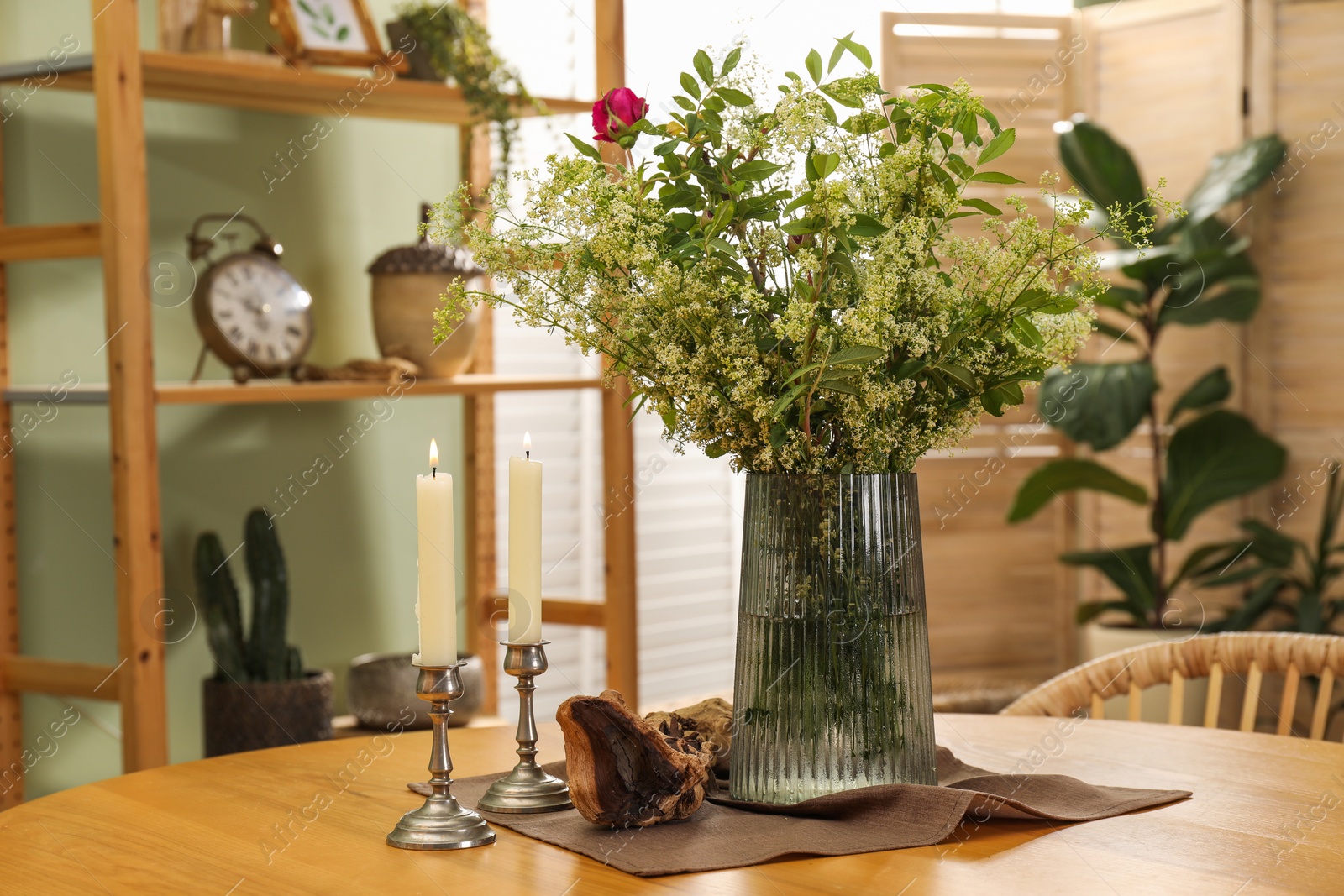 Photo of Vase with beautiful flowers and candles on wooden table in stylish dining room