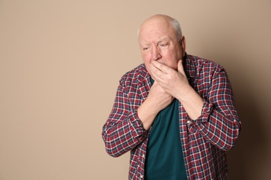 Senior man suffering from cough on color background. Space for text