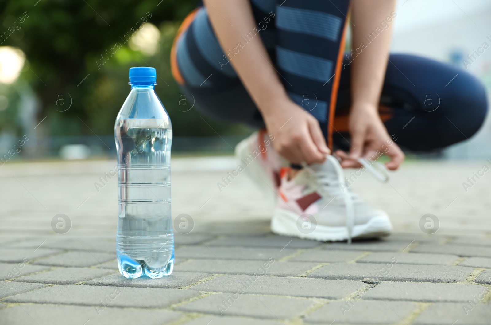 Photo of Closeup view of sportswoman lacing sneakers outdoors, focus on bottle with water