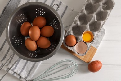 Photo of Fresh raw chicken eggs with colander, napkin and whisk on white wooden table, flat lay