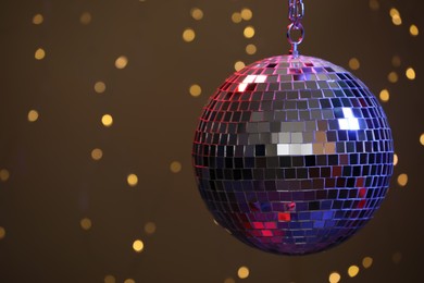 Photo of Shiny disco ball against blurred lights on brown background, space for text