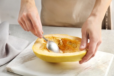 Photo of Woman scraping flesh of spaghetti squash with spoon on table, closeup