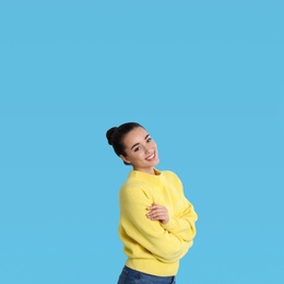 Beautiful young woman wearing yellow warm sweater on light blue background