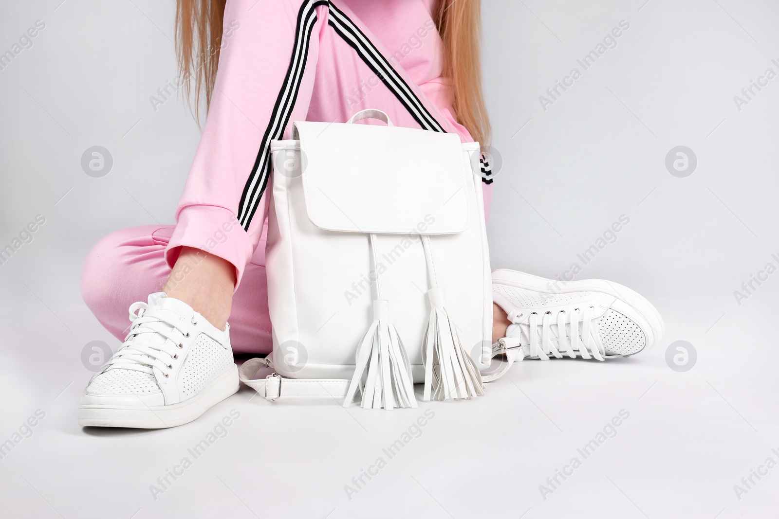 Photo of Woman in stylish sport shoes sitting with backpack on light background