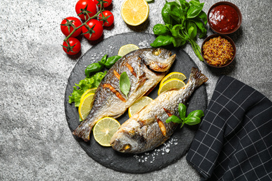 Photo of Delicious roasted fish with lemon on grey table, flat lay