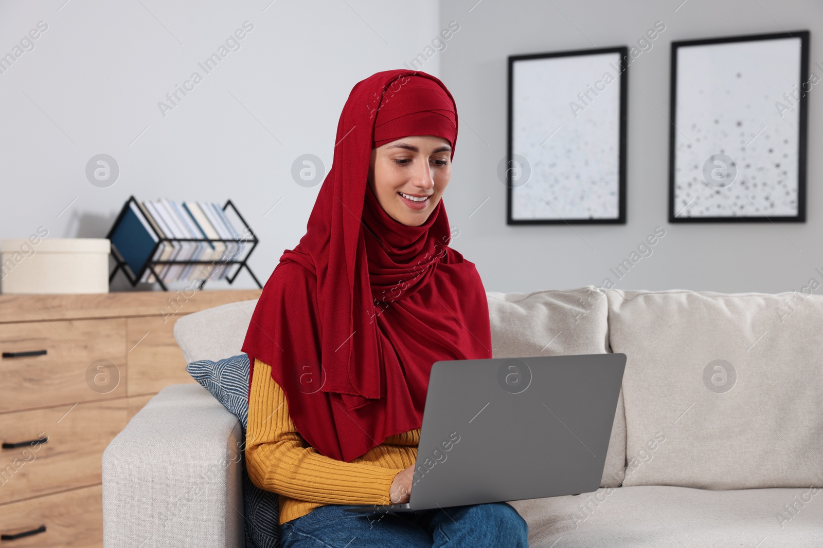 Photo of Muslim woman using laptop at couch in room