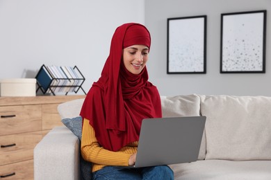 Muslim woman using laptop at couch in room