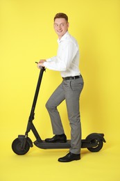 Happy man with modern electric kick scooter on yellow background