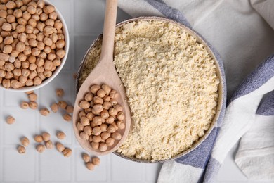 Photo of Chickpea flour in bowl and seeds on white tiled table, flat lay