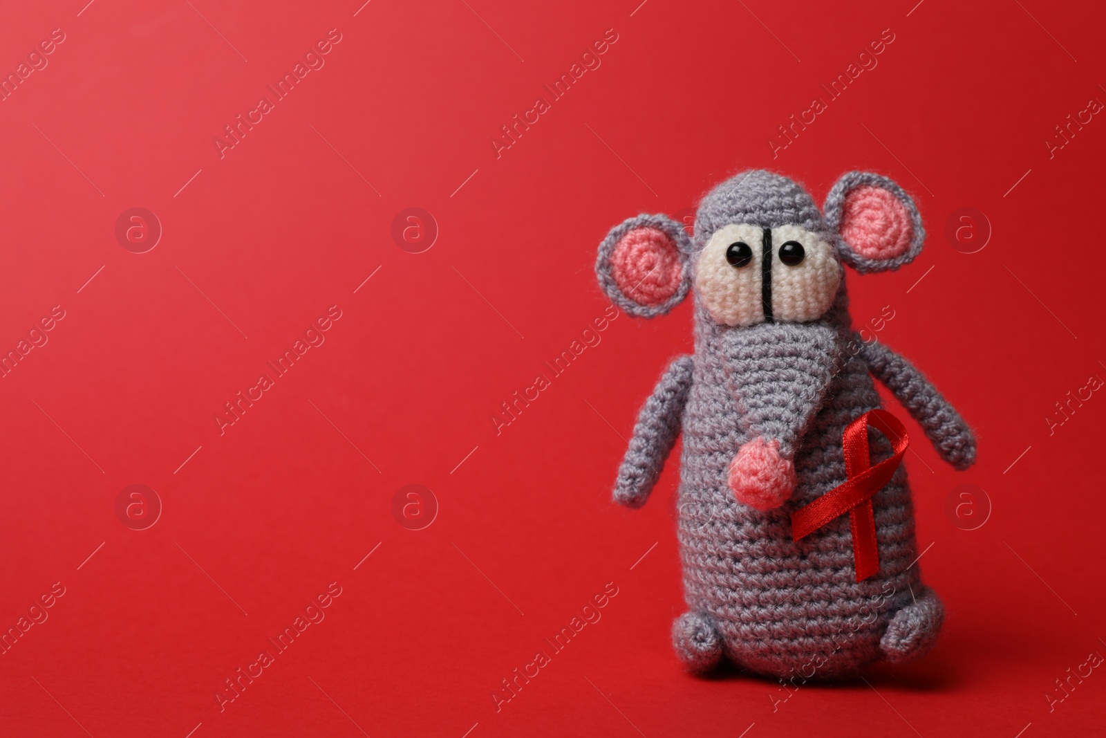 Photo of Cute knitted toy mouse with ribbon on red background, space for text. AIDS disease awareness