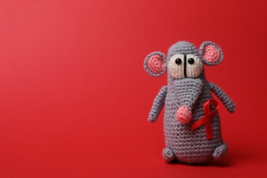 Cute knitted toy mouse with ribbon on red background, space for text. AIDS disease awareness