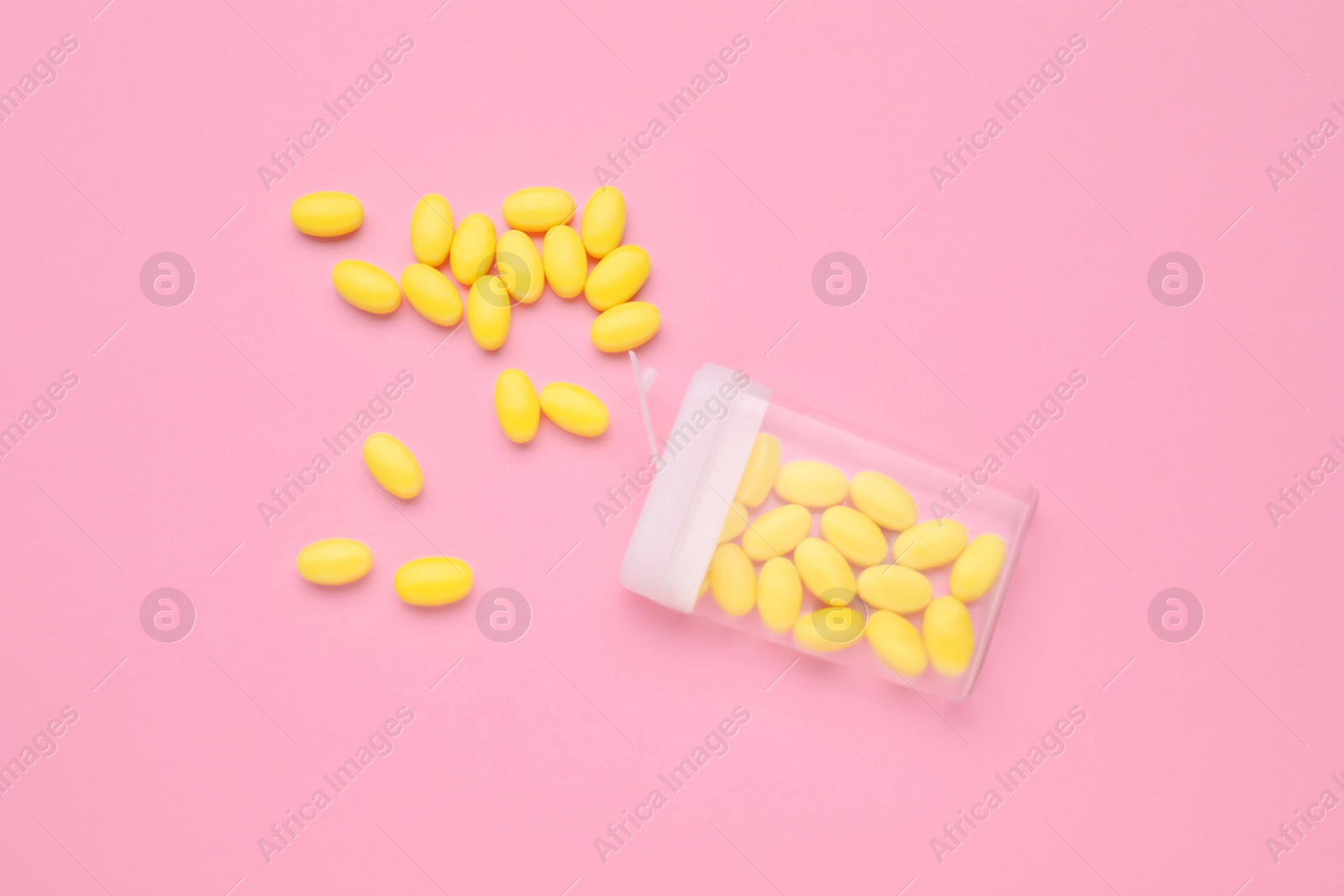 Photo of Yellow dragee candies and container on pink background, flat lay