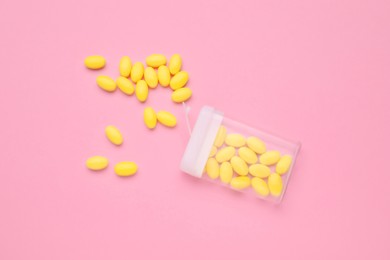 Yellow dragee candies and container on pink background, flat lay