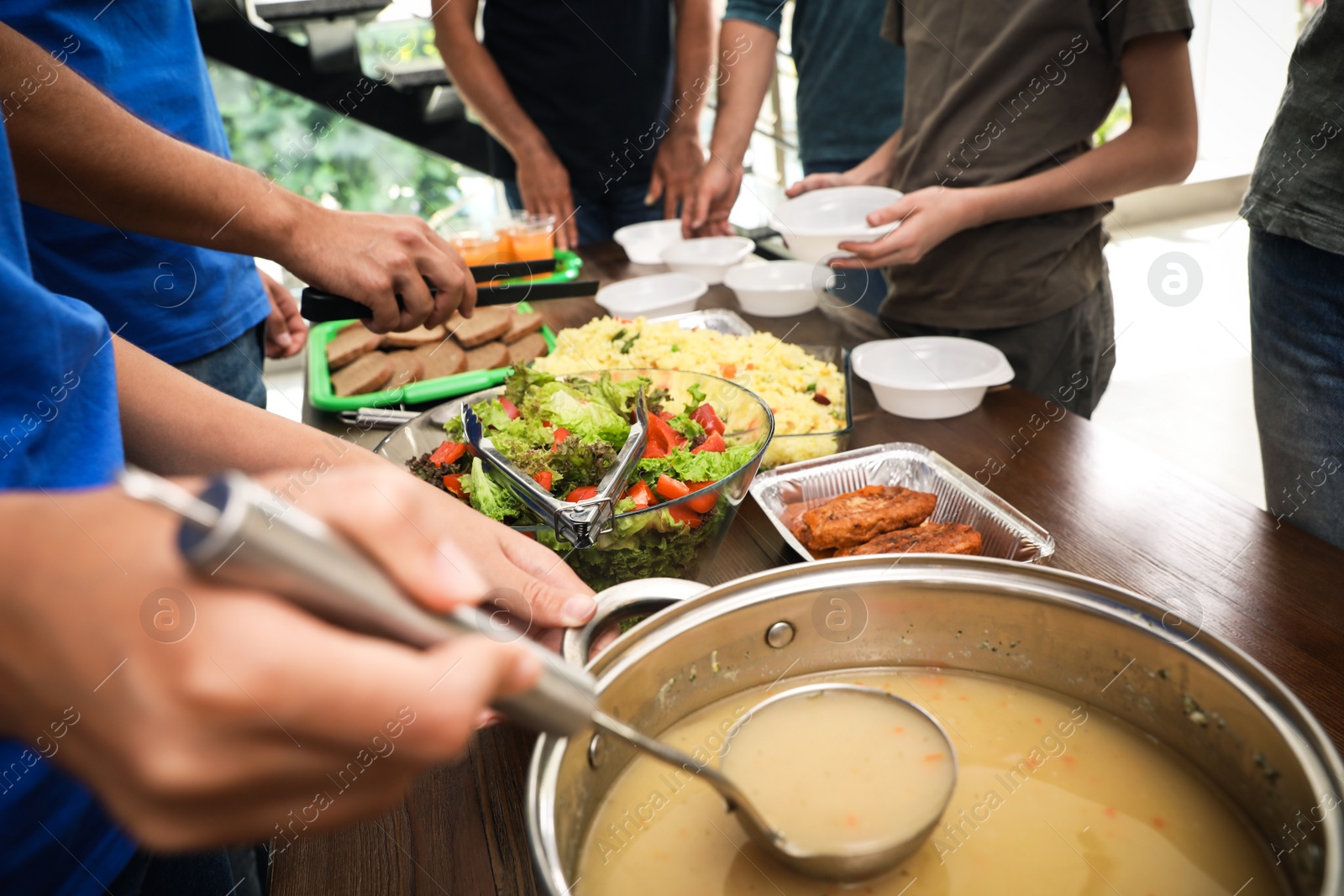 Photo of Volunteers serving food to poor people in charity centre, closeup