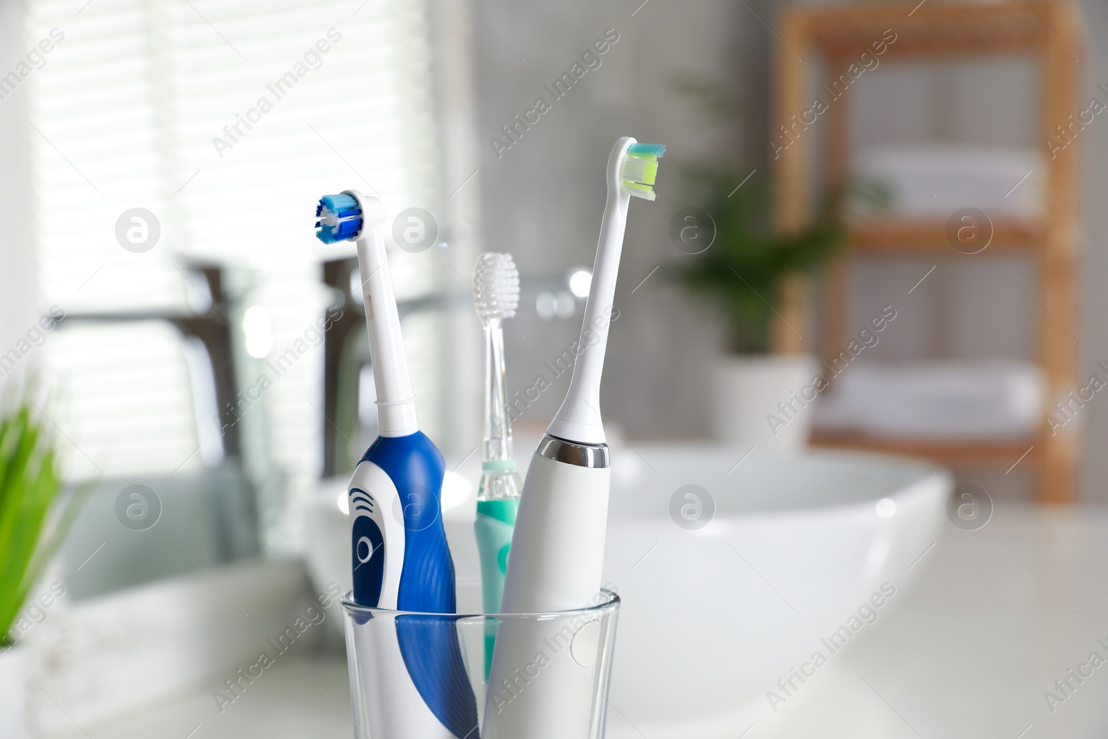 Photo of Electric toothbrushes in glass holder indoors, closeup